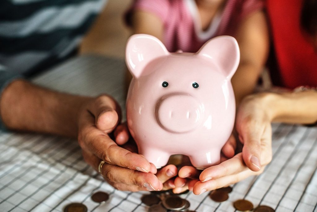 Two people holding a pink piggy bank and coins.